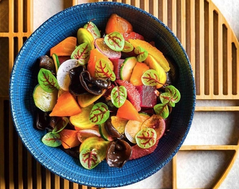 A colorful bowl of fruits and herbs is displayed on a wooden tray.