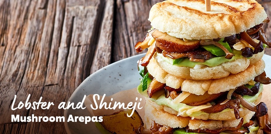 A professionally plated sandwich is shown. The text reads: Lobster and Shimeji Mushroom Arepas.
